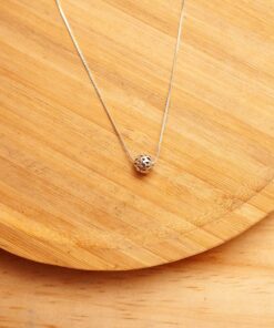 Foto do colar “Bola Mosaico”, acima de uma base de madeira rústica