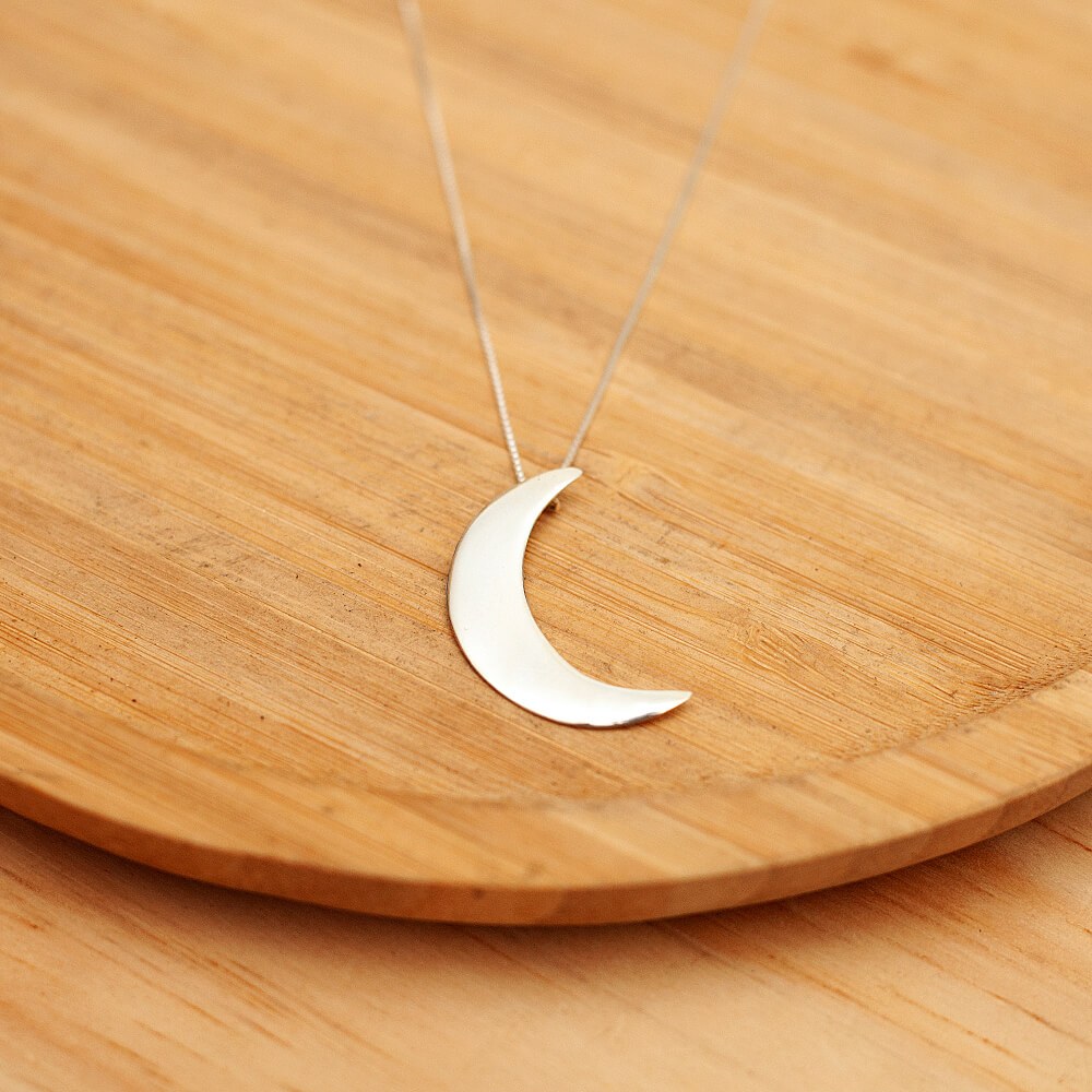 Foto do colar “Lua Lisa” tamanho G, acima de uma base de madeira rústica