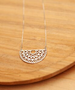 Foto do colar “Meia Mandala”, acima de uma base de madeira rústica