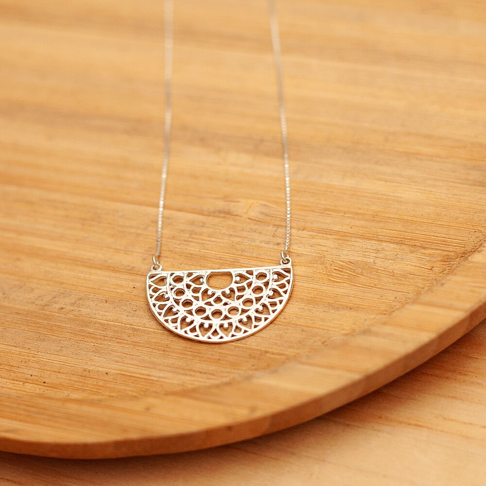 Foto do colar “Meia Mandala”, acima de uma base de madeira rústica