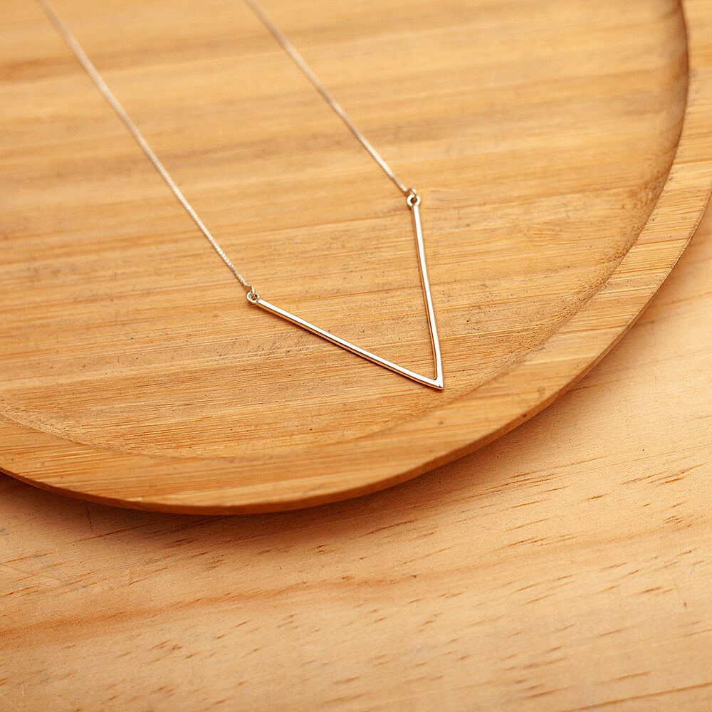 Foto do Colar V tamanho G, acima de uma base de madeira rústica