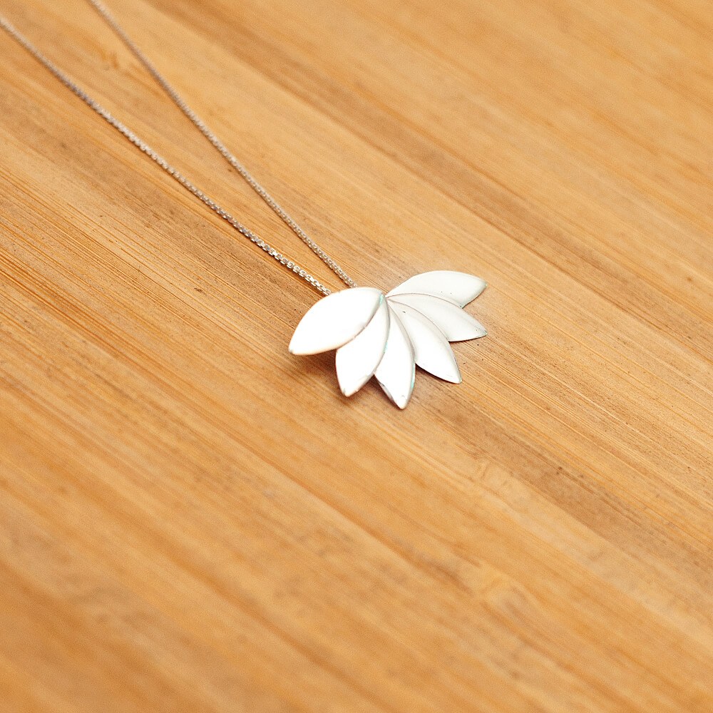 Foto do colar “Flor de lótus”, acima de uma base de madeira rústica